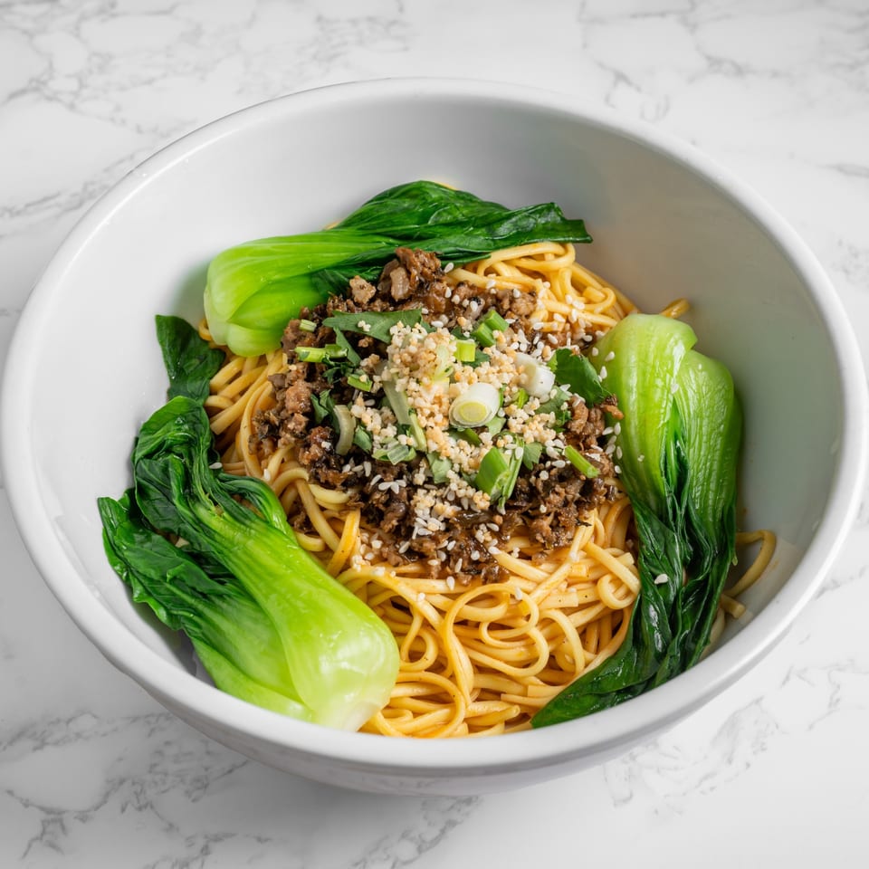 Nana Noodle House's Dan Dan noodles with minced pork, bok choy, and sesame seeds in a white bowl.