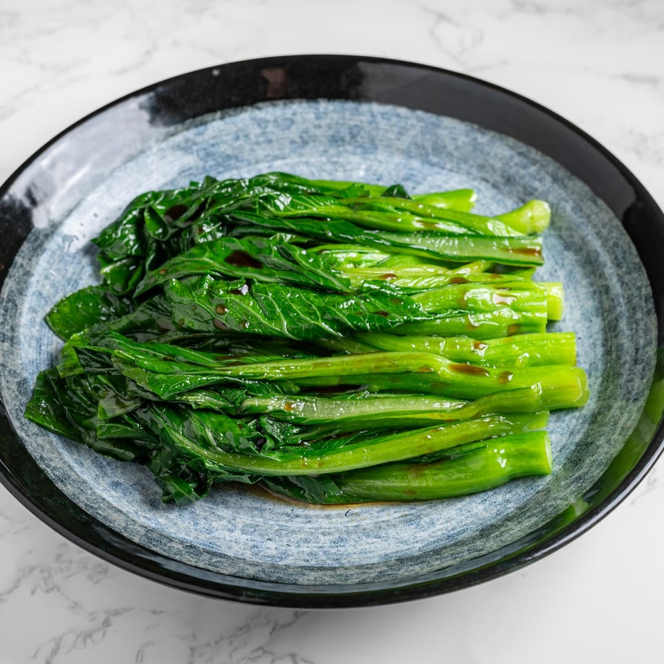 Nana Noodle House's vibrant green Chinese broccoli, glistening with sauce, served on a blue and black plate.
