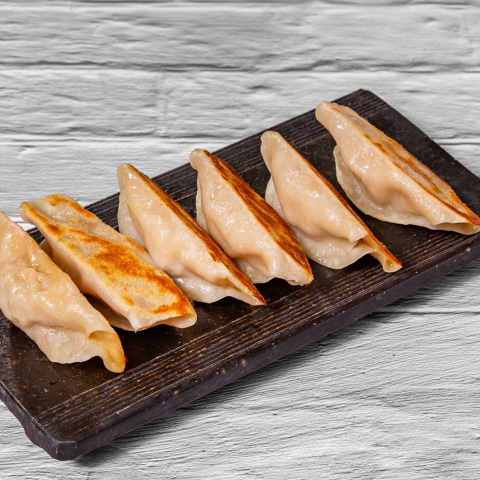 Six pan-fried Chinese dumplings with golden-brown bottoms on a dark rectangular plate.