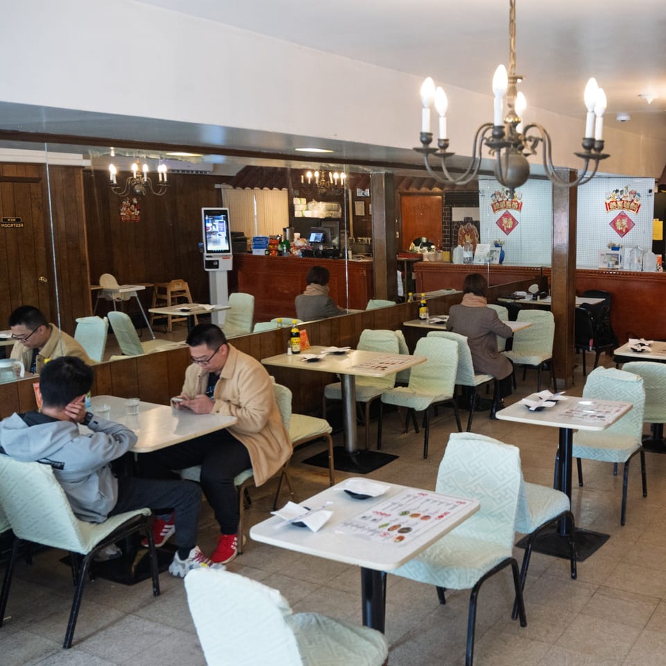 Diners seated at tables in Nana Noodle House, with mirrors reflecting the dining area and a chandelier.