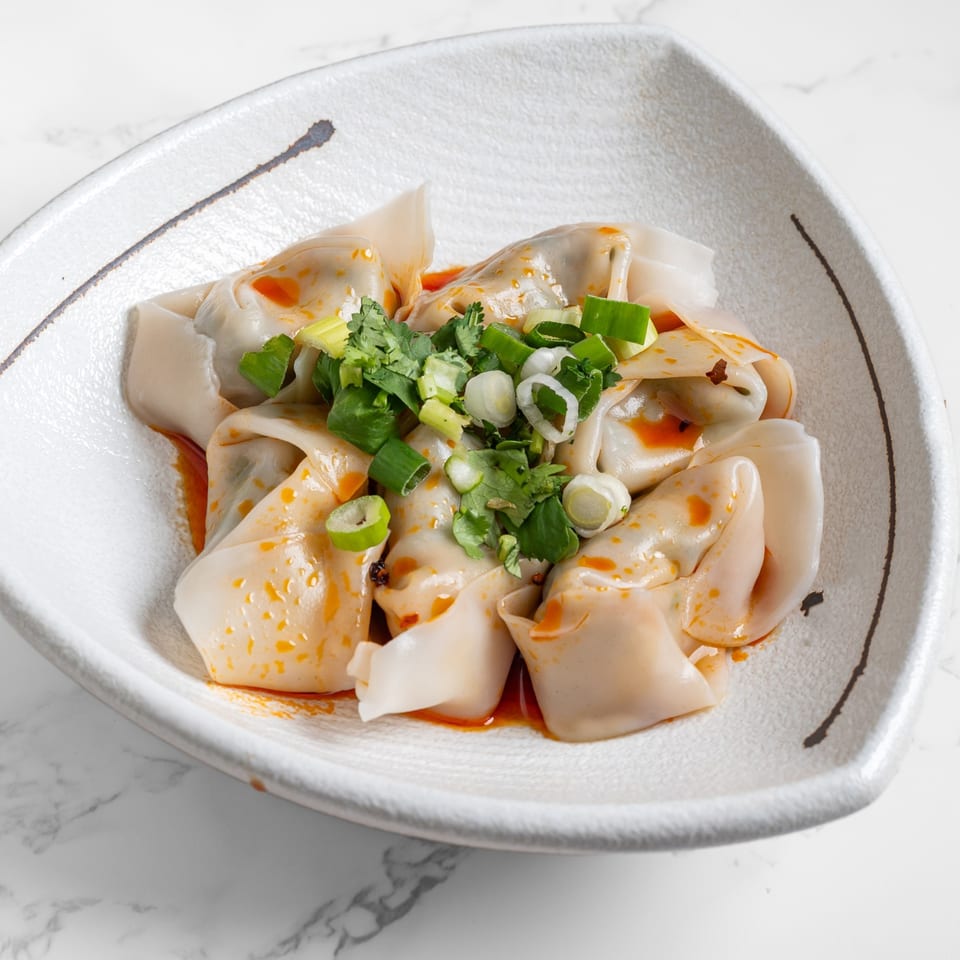 Nana Noodle House's chili oil wontons, garnished with fresh cilantro and green onions in a white bowl.