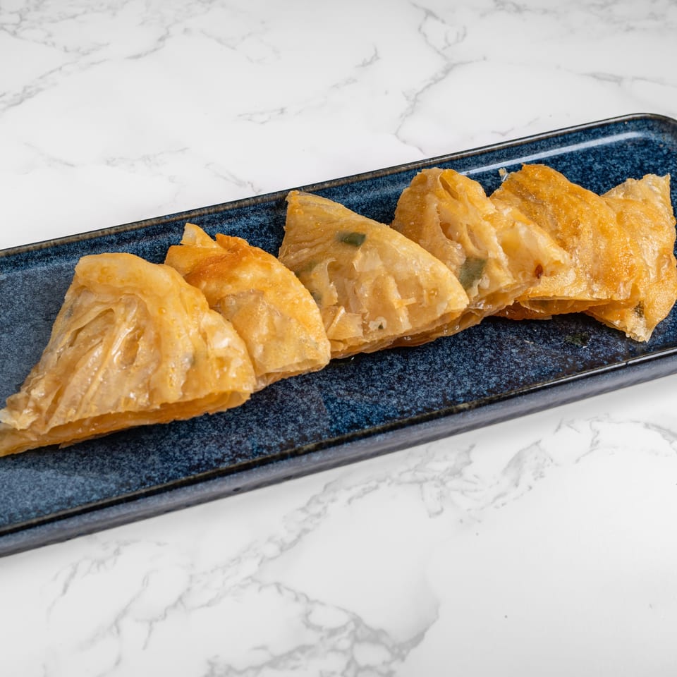 Five golden-brown, triangular fried dumplings, likely from Nana Noodle House, arranged on a dark blue rectangular plate.