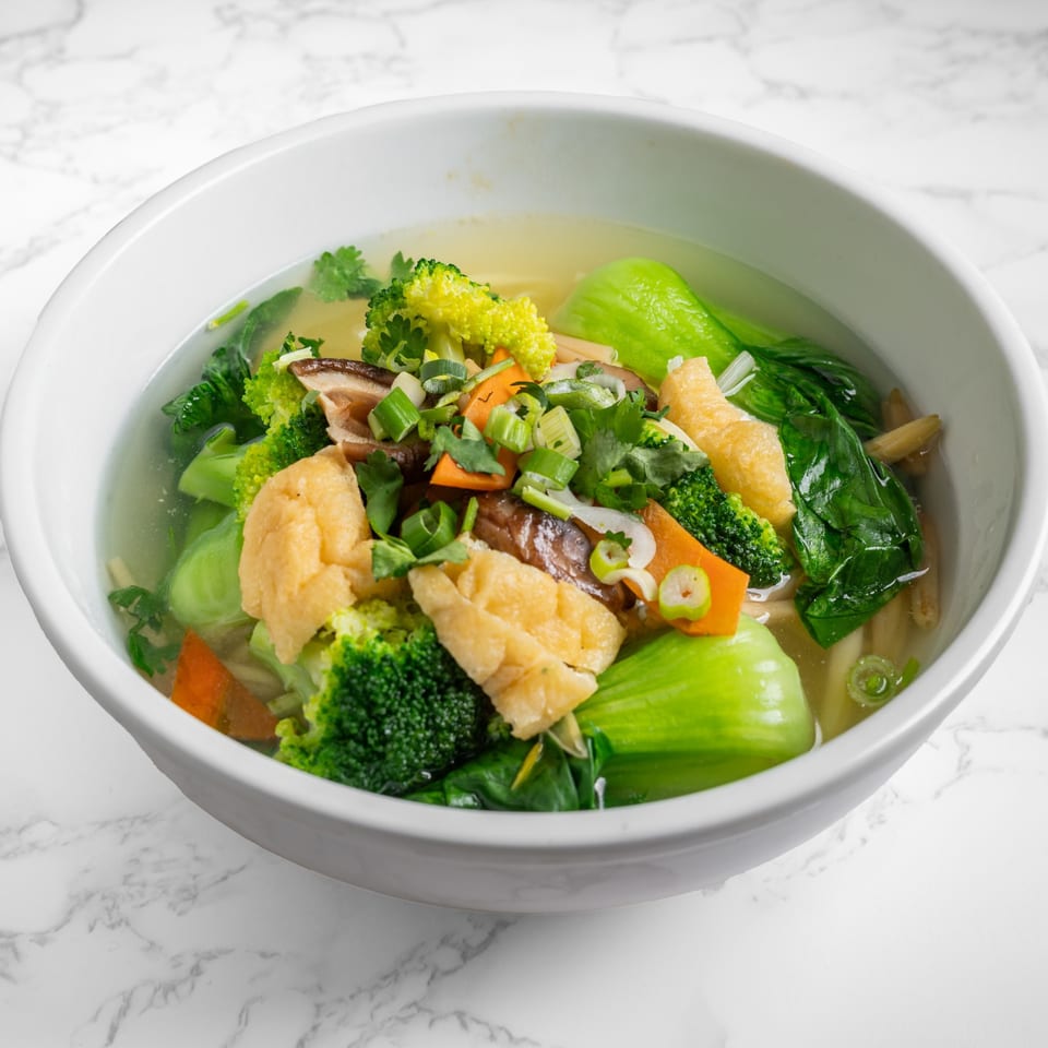 A white bowl of Nana Noodle House's vegetable noodle soup with broccoli, bok choy, and tofu.