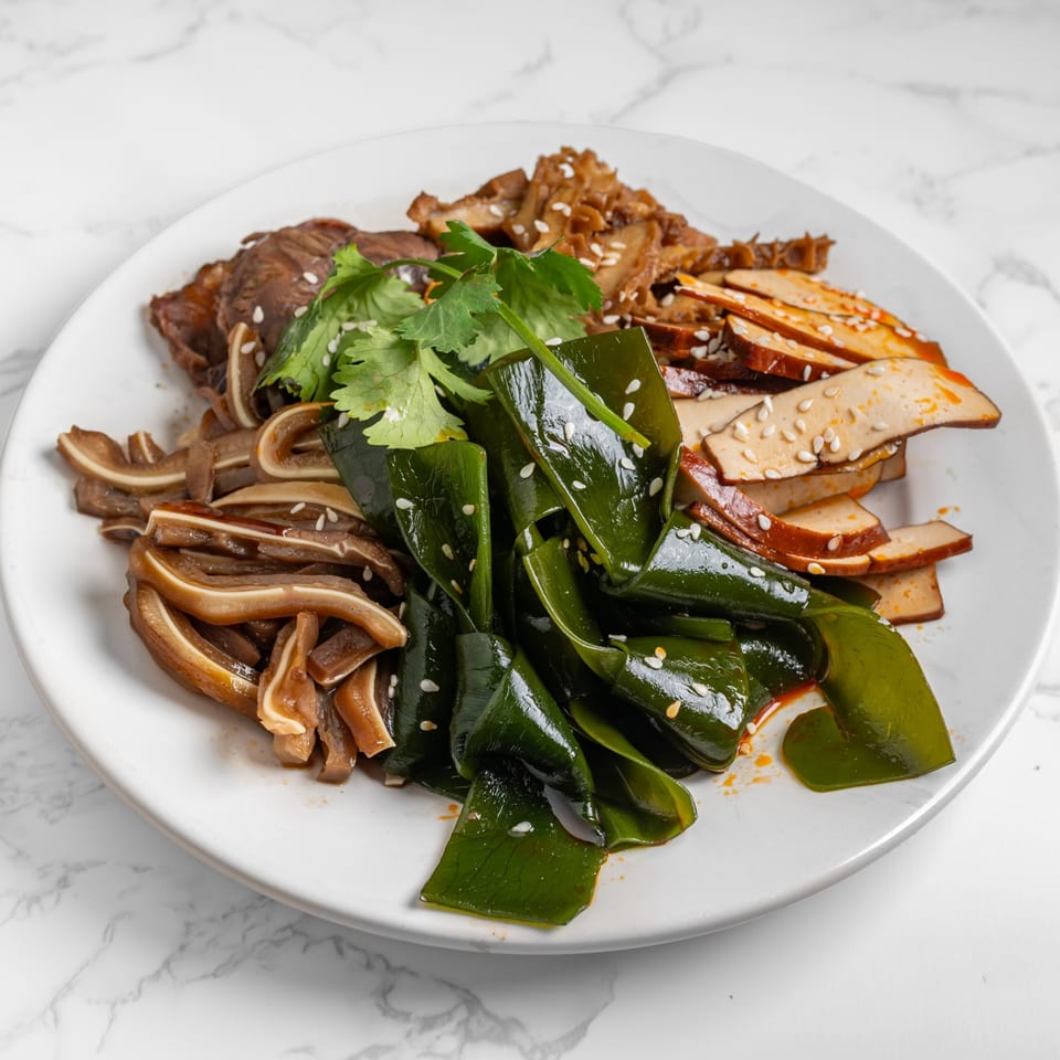 A white plate of Chinese cold appetizers including kelp, pig ears, beef, and tofu skin.