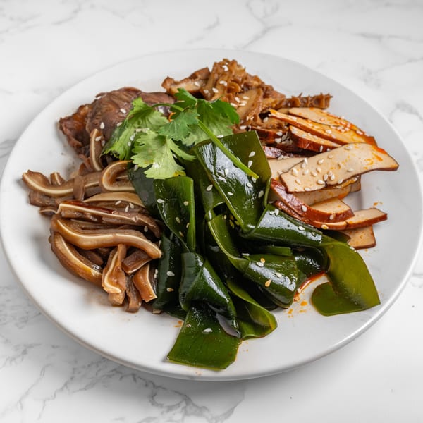 A white plate with various Chinese appetizers: sliced pork ear, beef, kelp, and tofu, garnished with cilantro.