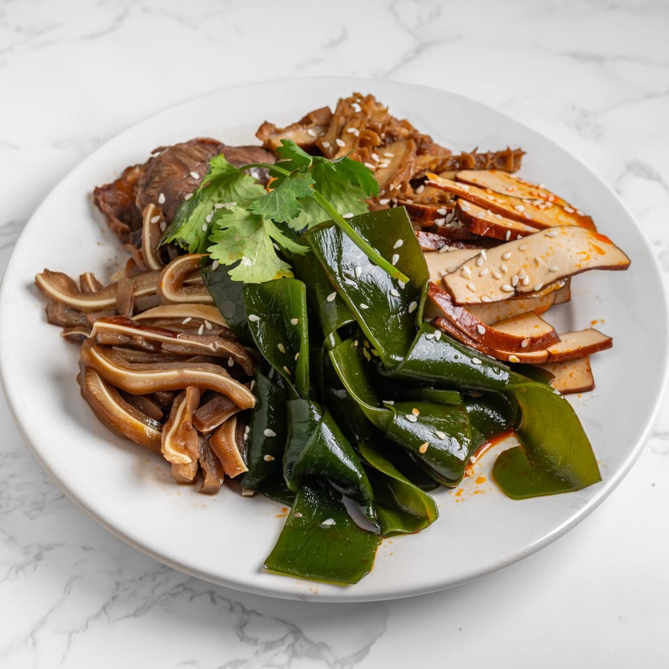 A white plate with various Chinese appetizers: sliced pork ear, beef, kelp, and tofu, garnished with cilantro.