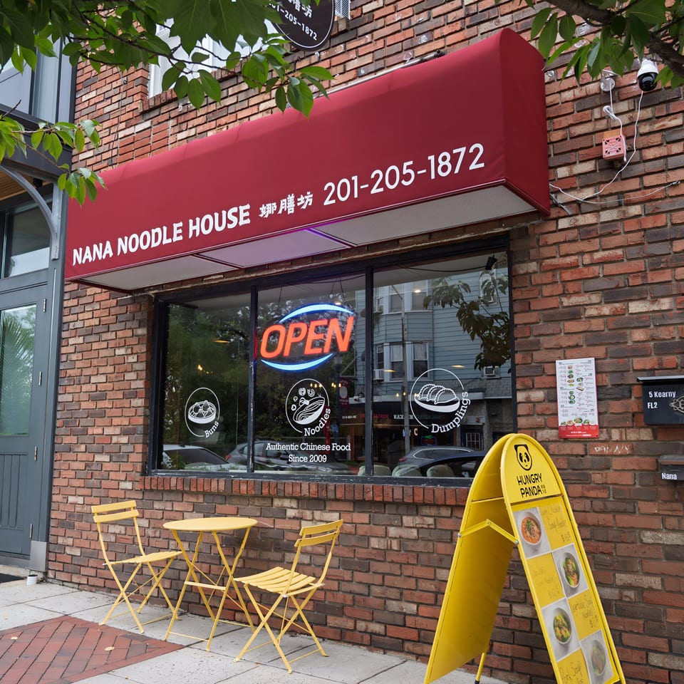 Exterior of Nana Noodle House, a Chinese restaurant, with a red awning, an "OPEN" sign, and yellow outdoor seating.