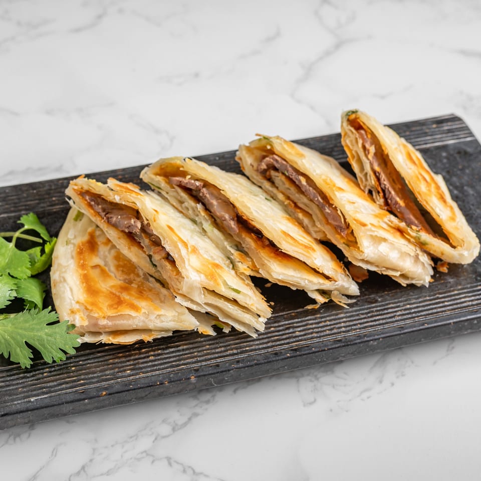 Crispy Chinese beef pancakes with cilantro on a dark wooden board.